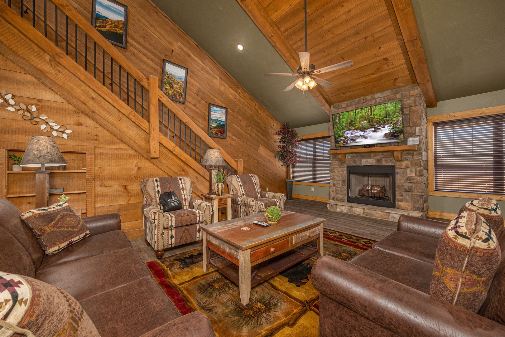 Heaps of Fun cabin living room — vaulted cedar ceiling, stone gas fireplace, rustic leather seating, and mountain-themed decor at Laurel Estates