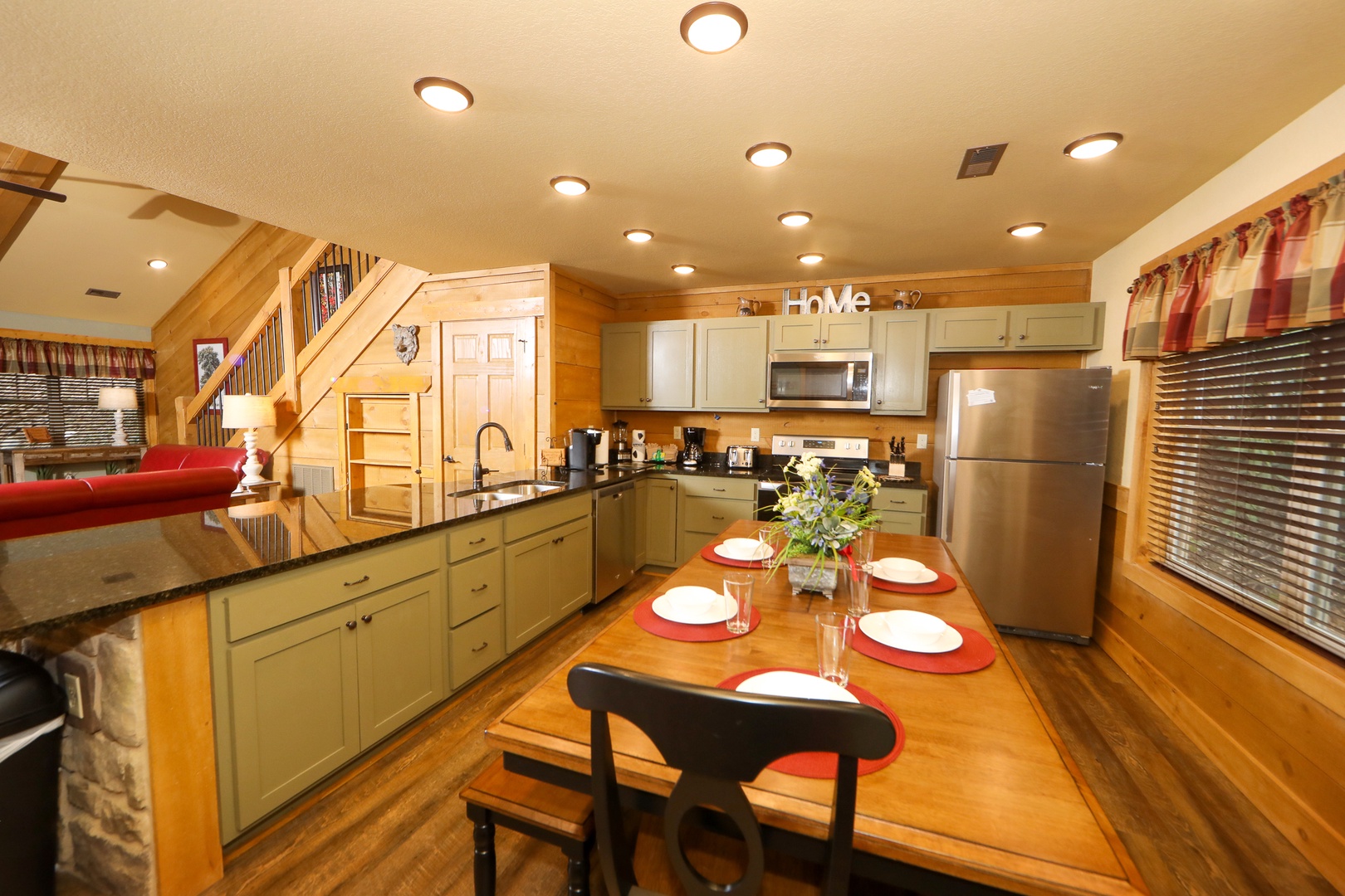 Ivie Holler open kitchen — sage green cabinetry, granite countertops, stainless appliances, and farmhouse dining table at Laurel Estates